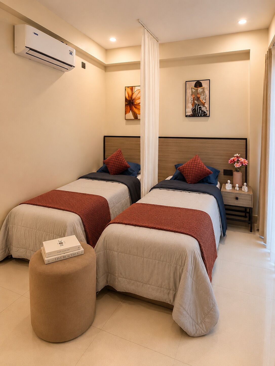 Quarto de hotel com duas camas, um banquinho redondo, uma mesa de cabeceira com um vaso e obras de arte nas paredes.