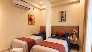 Habitación de hotel con dos camas, una mesita de noche con un florero y un equipo de aire acondicionado en la pared.