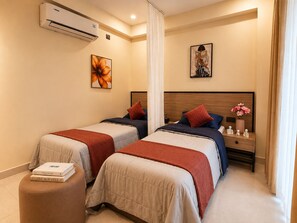 A hotel room with two beds, a nightstand with a vase of flowers, and an air conditioning unit on the wall. - C Suites Maclean (Bengaluru)