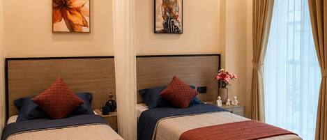 A hotel room with two beds, a nightstand, a round ottoman, and artwork on the walls.