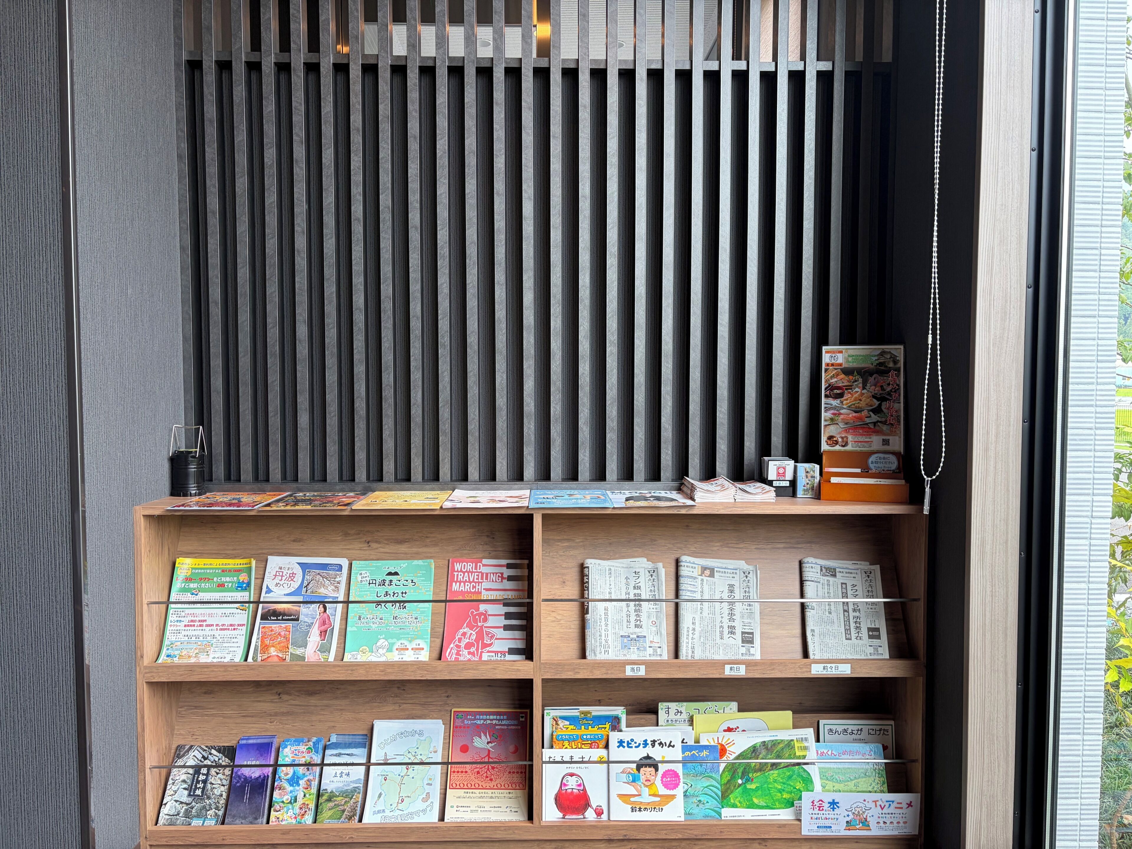 Una estantería con varios libros y revistas, una celosía de metal negro y una puerta de madera.