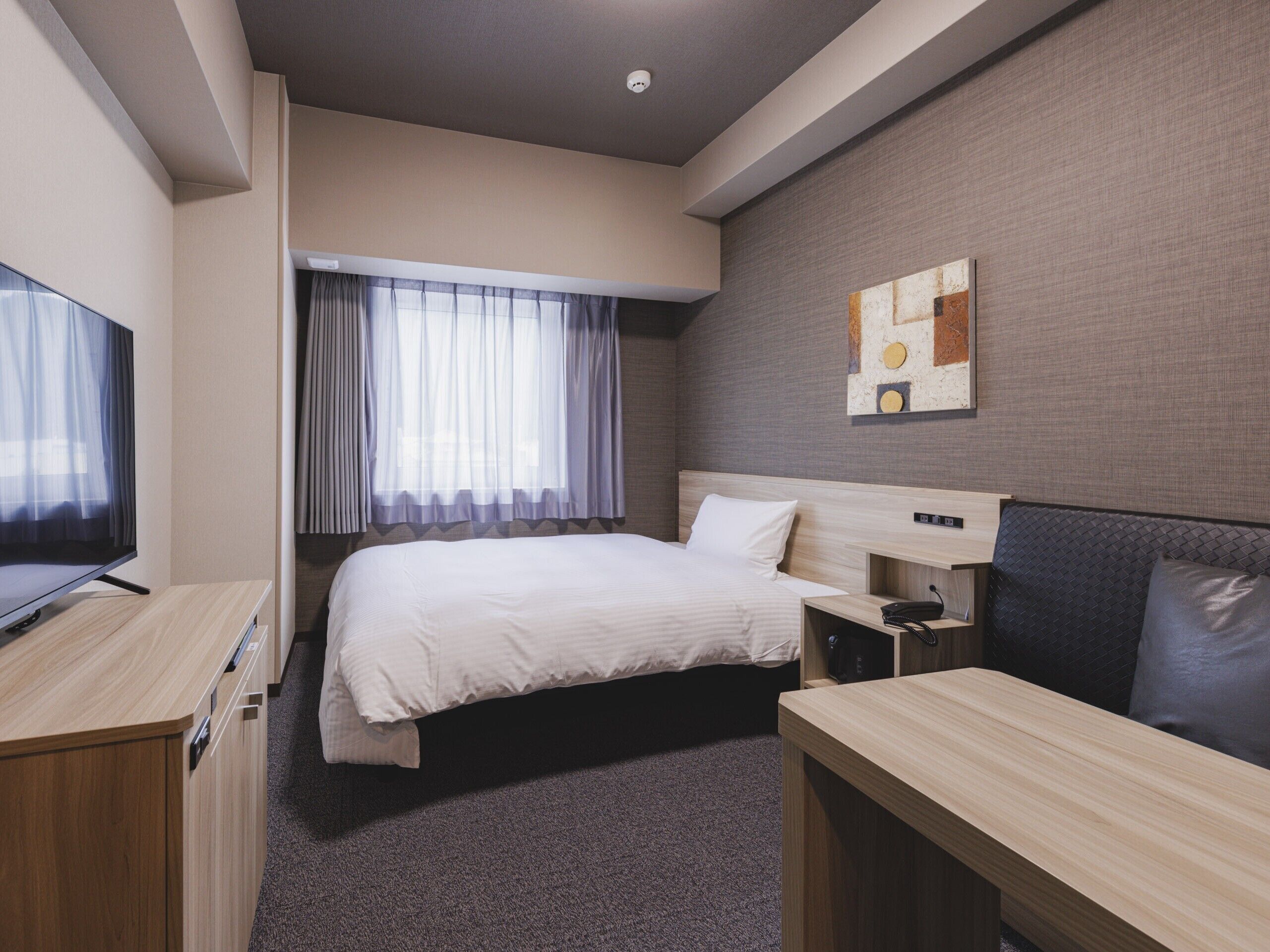 A hotel room with a bed, a desk, a television, and a window with curtains.