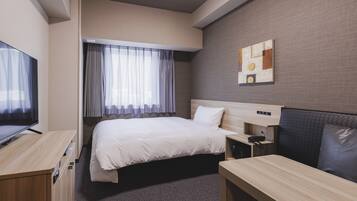 A hotel room with a bed, a desk, a television, and a window with curtains.