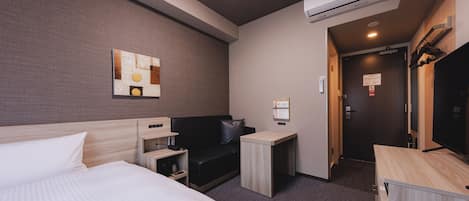 A hotel room with a bed, a desk, a chair, a TV, and an air conditioning unit.