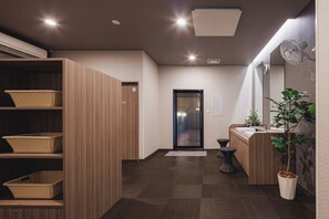Un hall de hotel con mostrador de recepción, una planta, cestas de mimbre y un armario de madera.