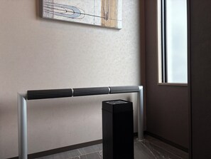 Un interior moderno con un mueble consola minimalista y un objeto negro y alto, posiblemente un altavoz, frente a una pared con textura y una ventana.