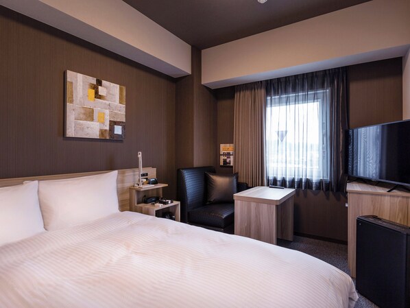 Habitación de hotel con una cama grande, un escritorio, una silla, un televisor y una ventana con cortinas.