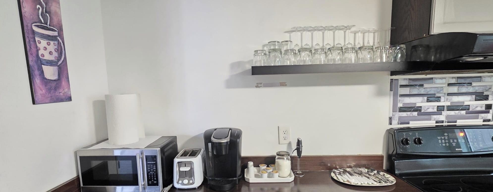 Cozinha equipada com micro-ondas, torradeira, cafeteira e um prato de talheres.