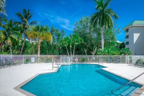 An outdoor swimming pool and sun deck surrounded by palm trees and a white fence. - Key West Paradise Condo w/ Pool, Hot Tub, Tennis (Key West)