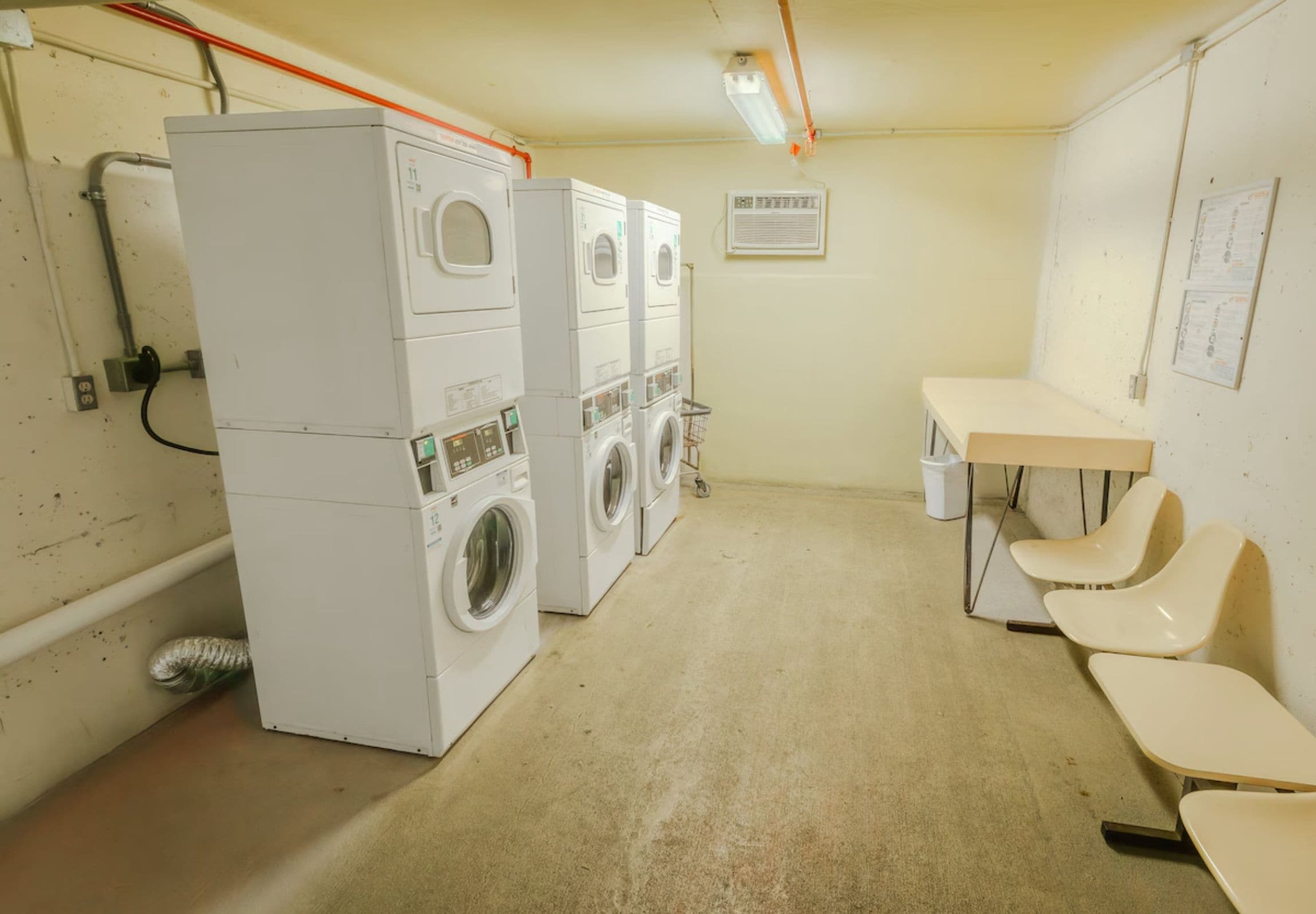 Une buanderie équipée d’une machine à laver et d’un sèche-linge superposés, d’une table, de chaises et d’un climatiseur fixé au mur.
