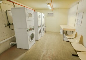 Une buanderie équipée d’une machine à laver et d’un sèche-linge superposés, d’une table, de chaises et d’un climatiseur fixé au mur.