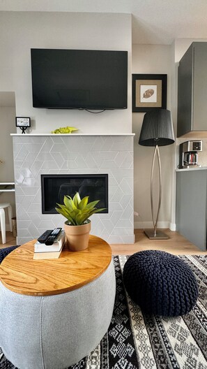 A modern living room with a fireplace, a mounted TV, and a coffee machine. - The Canmore Mountain Twin Retreat with 4BR • 2 Homes • Heated Pool & Hot Tub (Canmore)