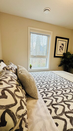 A bedroom with a bed, pillows, a window, and a framed botanical print on the wall. - The Canmore Mountain Twin Retreat with 4BR • 2 Homes • Heated Pool & Hot Tub (Canmore)