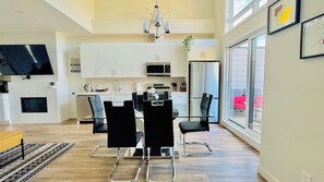 A modern kitchen with white cabinets, a microwave, and a dining area with black chairs and a glass table. - The Canmore Mountain Twin Retreat with 4BR • 2 Homes • Heated Pool & Hot Tub (Canmore)