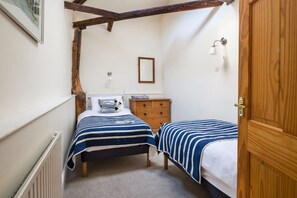 Ein Schlafzimmer mit zwei Betten, einer hölzernen Kommode, einem Heizkörper, einem gerahmten Spiegel und einer Wandleuchte.