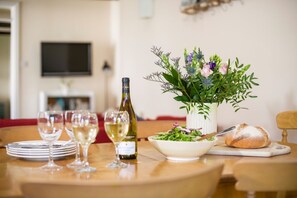 Una mesa de comedor con una botella de vino blanco, copas, un cuenco de ensalada y una hogaza de pan.