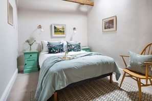 Un dormitorio con una cama, una mesita de noche, una silla y una lámpara de pared.