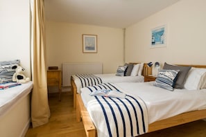 Ein Hotelzimmer mit zwei Betten, einem Nachttisch mit Lampe, einem Heizkörper und einem Fenster mit Vorhängen.