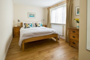 A bedroom with a wooden bed, a nightstand, a dresser, and a window with curtains. - Rose Cottage - sleeps 4 guests  in 2 bedrooms (Port Gaverne)