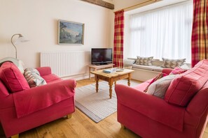 Ein Wohnzimmer mit zwei roten Sofas, einem Holztisch, einem Fernseher und einem Fenster mit Vorhängen.