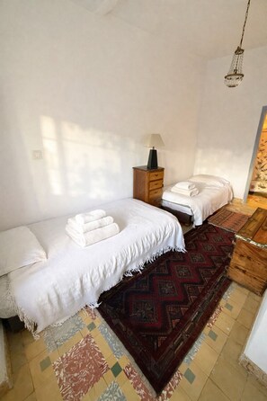 Ein Schlafzimmer mit zwei Betten, einem Nachttisch mit Lampe, einem gemusterten Teppich und einer Pendelleuchte.