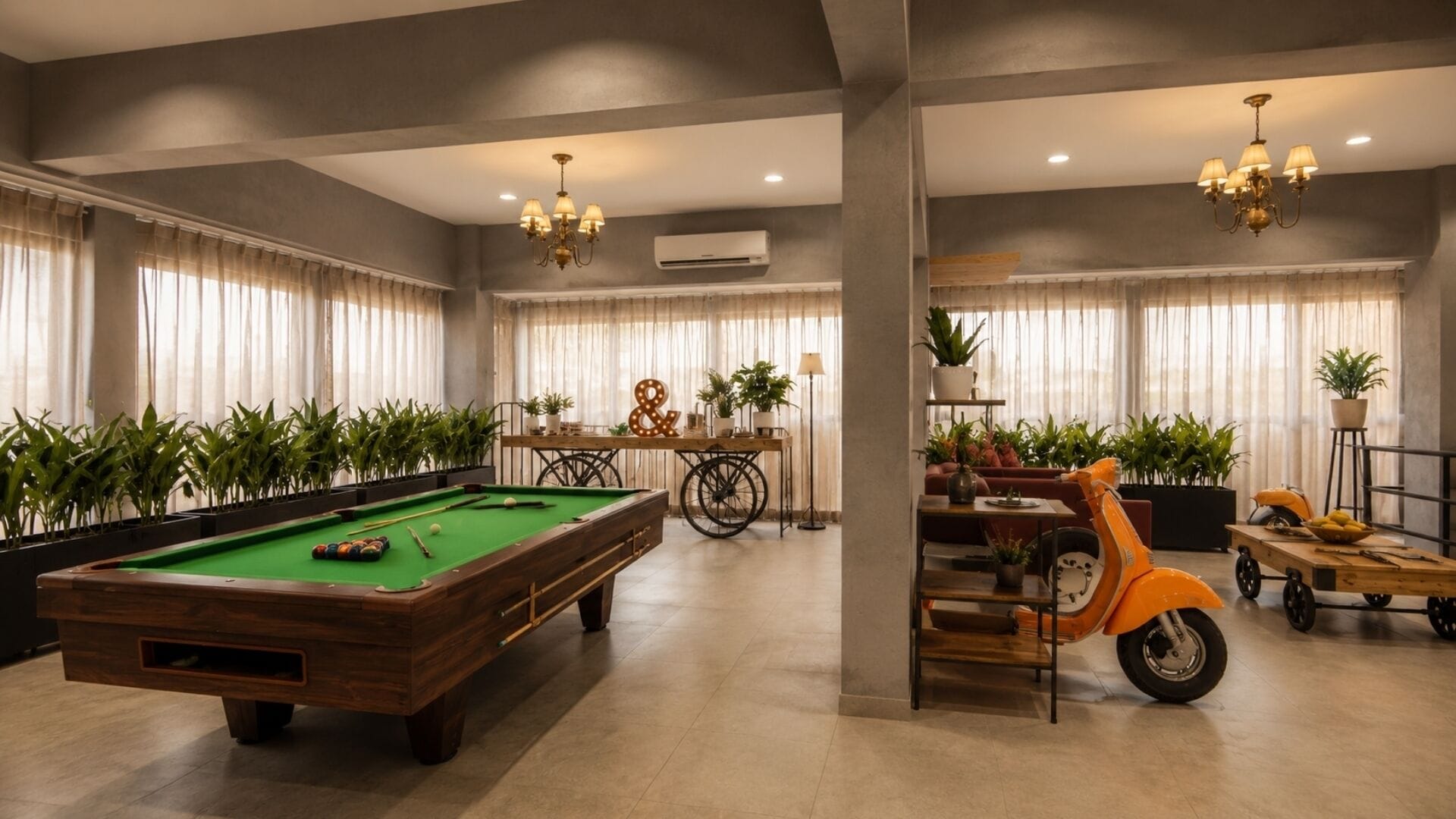 Una mesa de billar, una bicicleta y un patinete en una habitación con ventanas amplias y plantas.