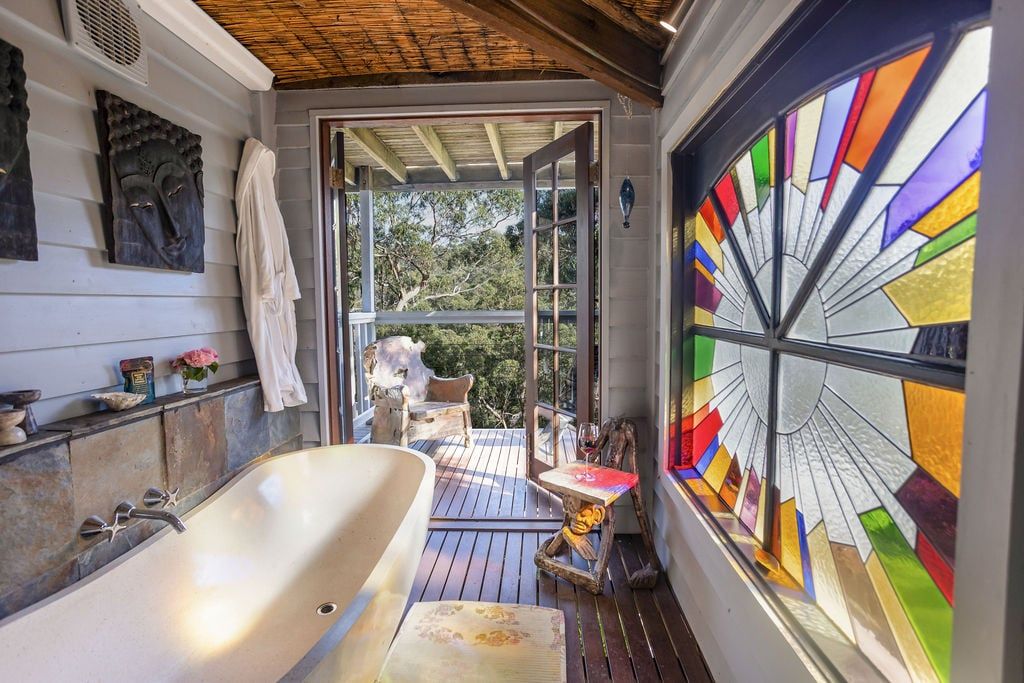 A bathroom with a freestanding bathtub, a wooden deck, and a stained glass window.