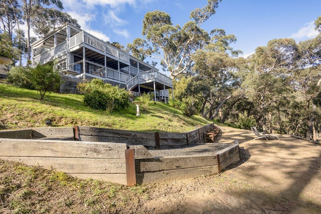 A two-story house with a balcony, surrounded by trees and a landscaped garden.
