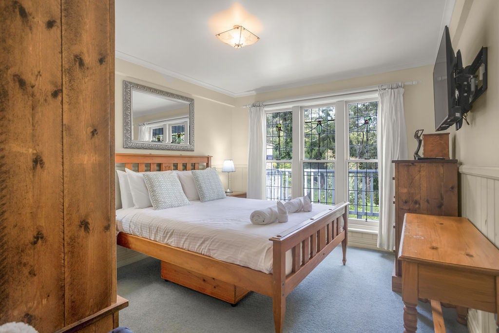 Un dormitorio con una cama de madera, una mesita de noche, un aparador, un espejo y una ventana con vistas a zonas verdes.