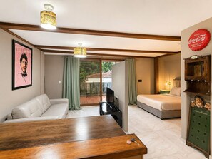 A hotel room with a wooden table, a sofa, a bed, a television, and a Coca-Cola sign. - Central Bella Vista Apt w/ Terrace & Fast WiFi (Panama City)