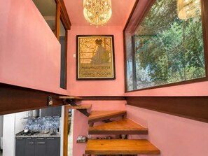 Una escalera con escalones de madera que conduce a un rellano, un candelabro y una obra de arte enmarcada en la pared.