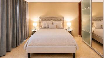 Habitación de hotel con una cama grande, dos mesitas de noche con lámparas, un armario con espejo y un ventanal cubierto con cortinas.