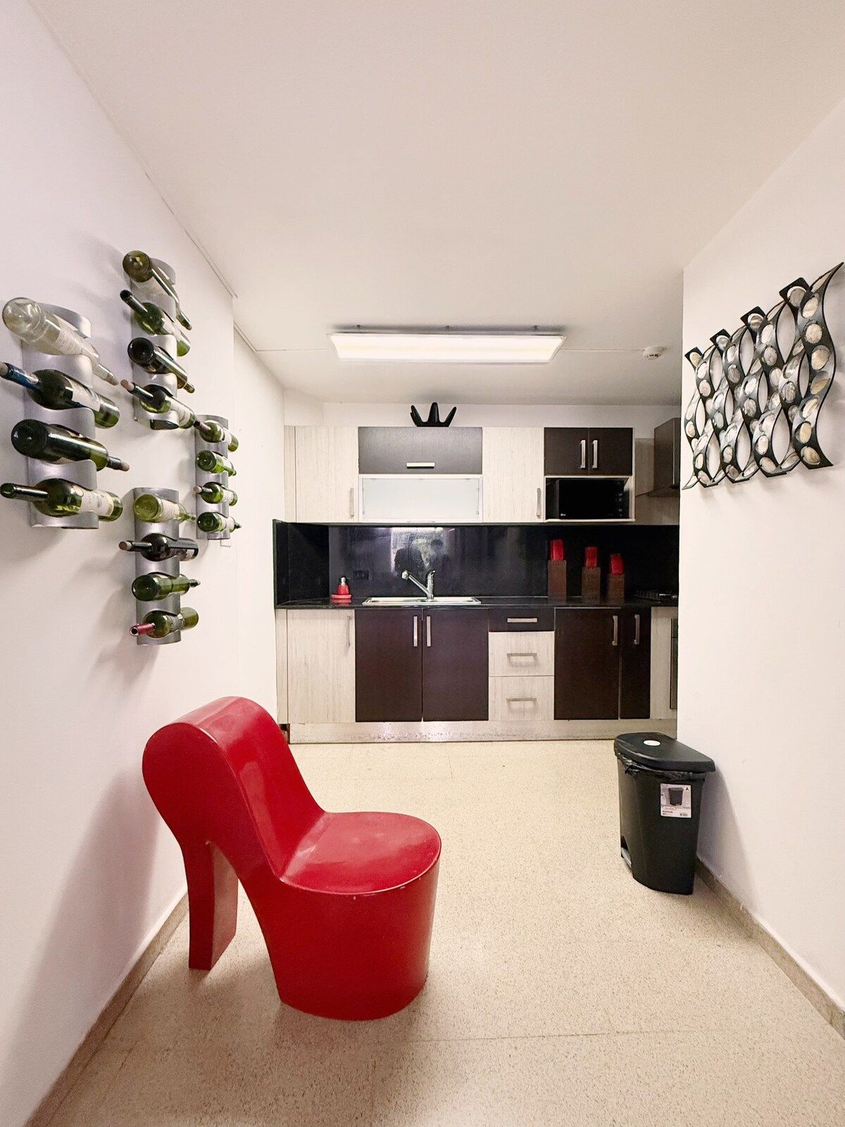 A modern kitchen with a wine rack, a red chair, and a trash bin.