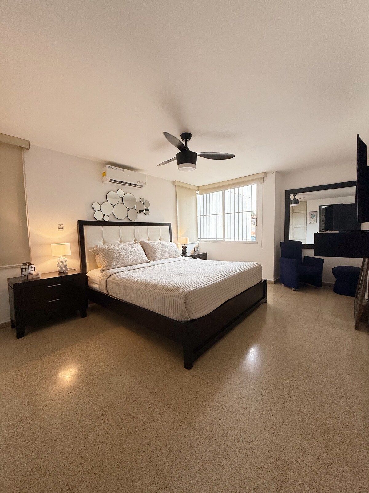 A bedroom with a bed, bedside tables, a ceiling fan, a window, and a TV.