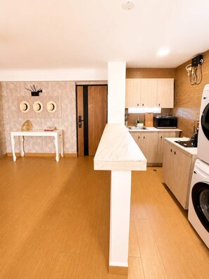 A modern kitchen with wooden cabinets, a microwave, and a washing machine. - Skyline Views Casco Viejo Apt | Historic (Panamá)