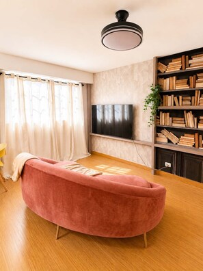 A living room with a pink sofa, a flat-screen TV, a bookshelf, and a ceiling light fixture. - Skyline Views Casco Viejo Apt | Historic (Panamá)