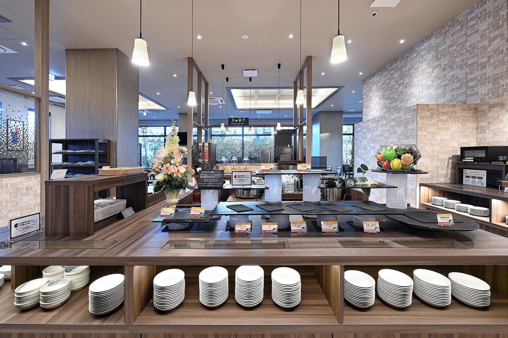 A modern restaurant interior with a central counter, multiple seating areas, and a brick wall.