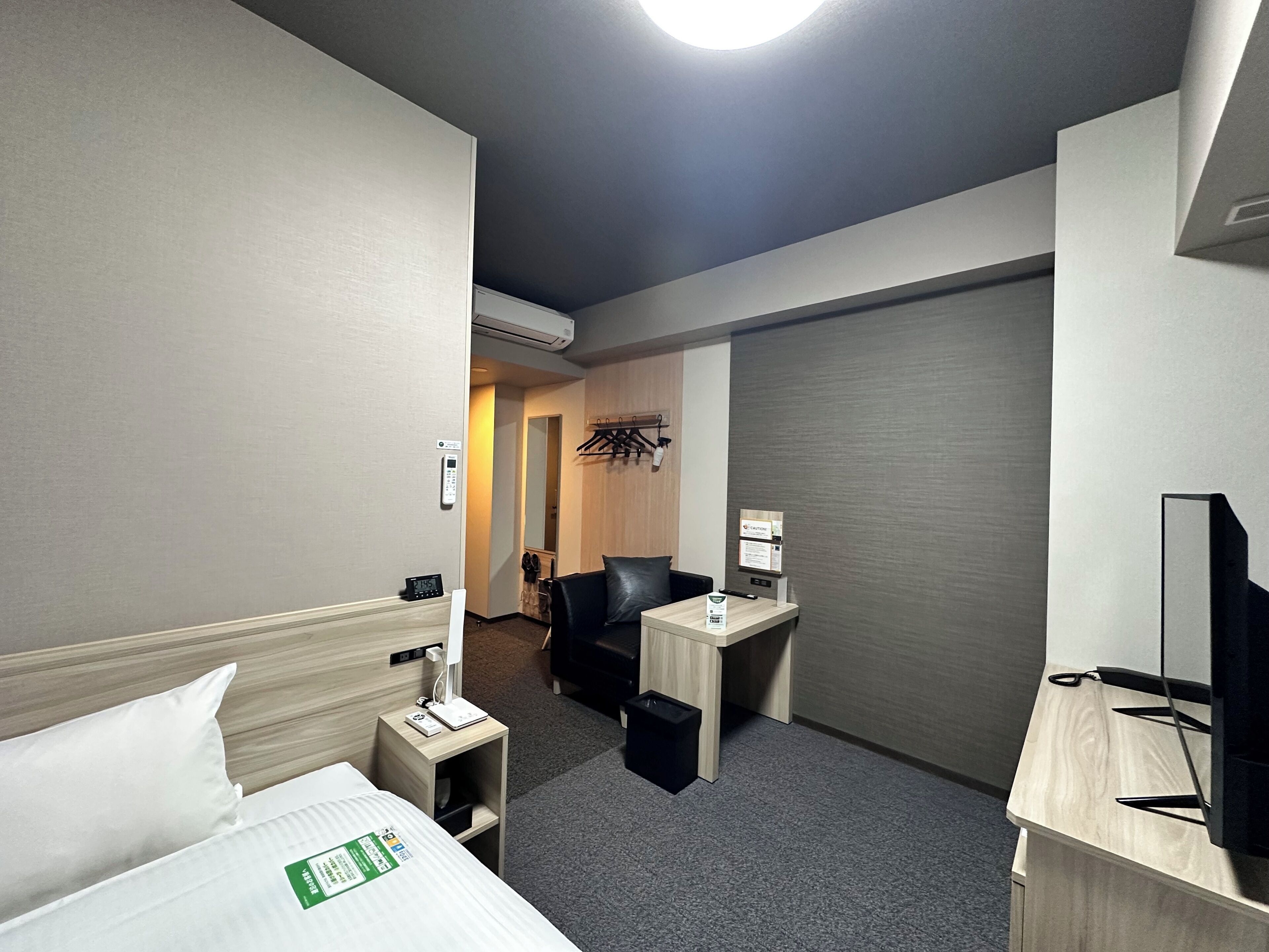 A hotel room with a bed, a desk, a chair, a TV, and a mirror.
