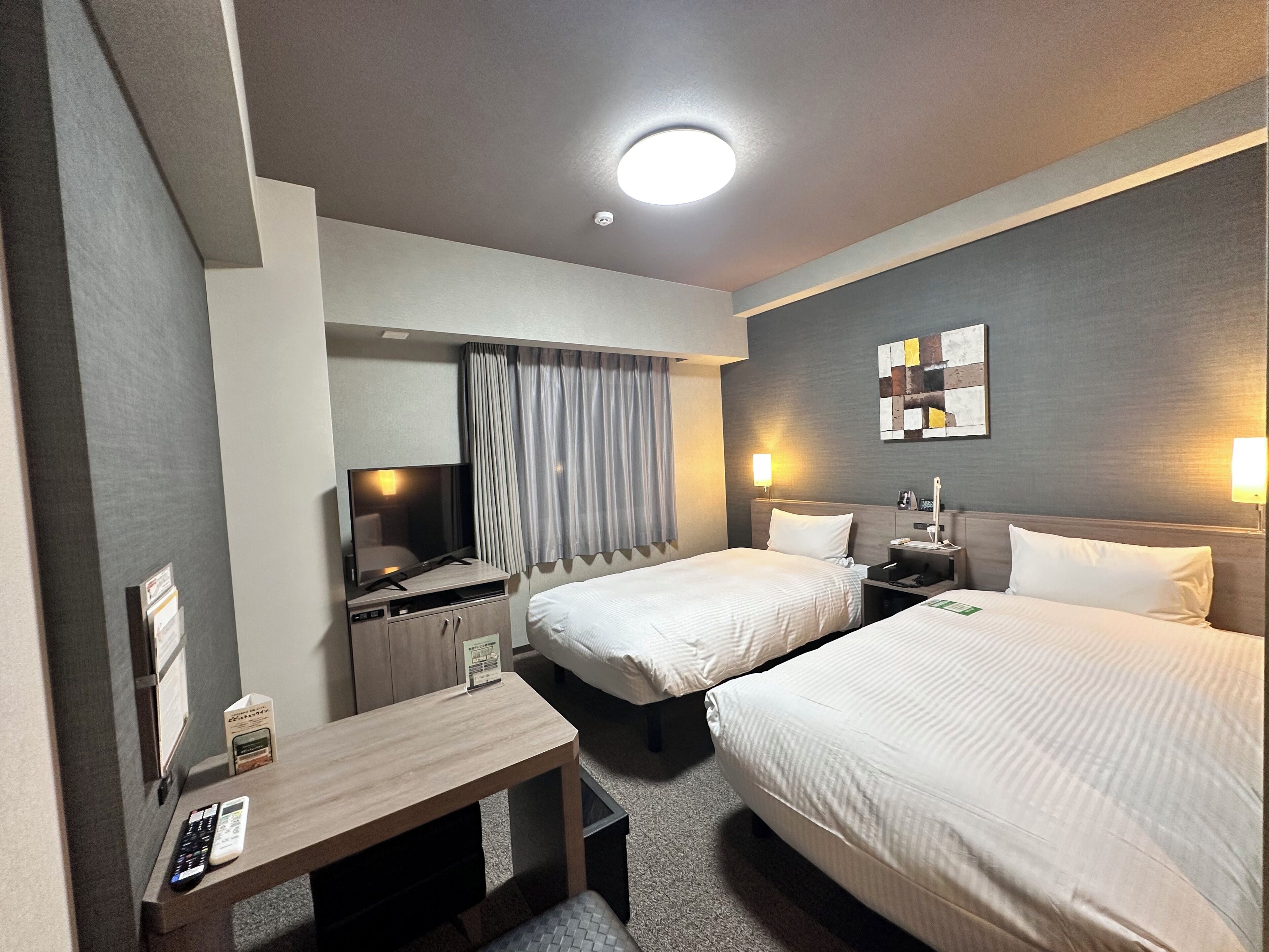 A hotel room with two beds, a desk, a TV, and a wall-mounted artwork.