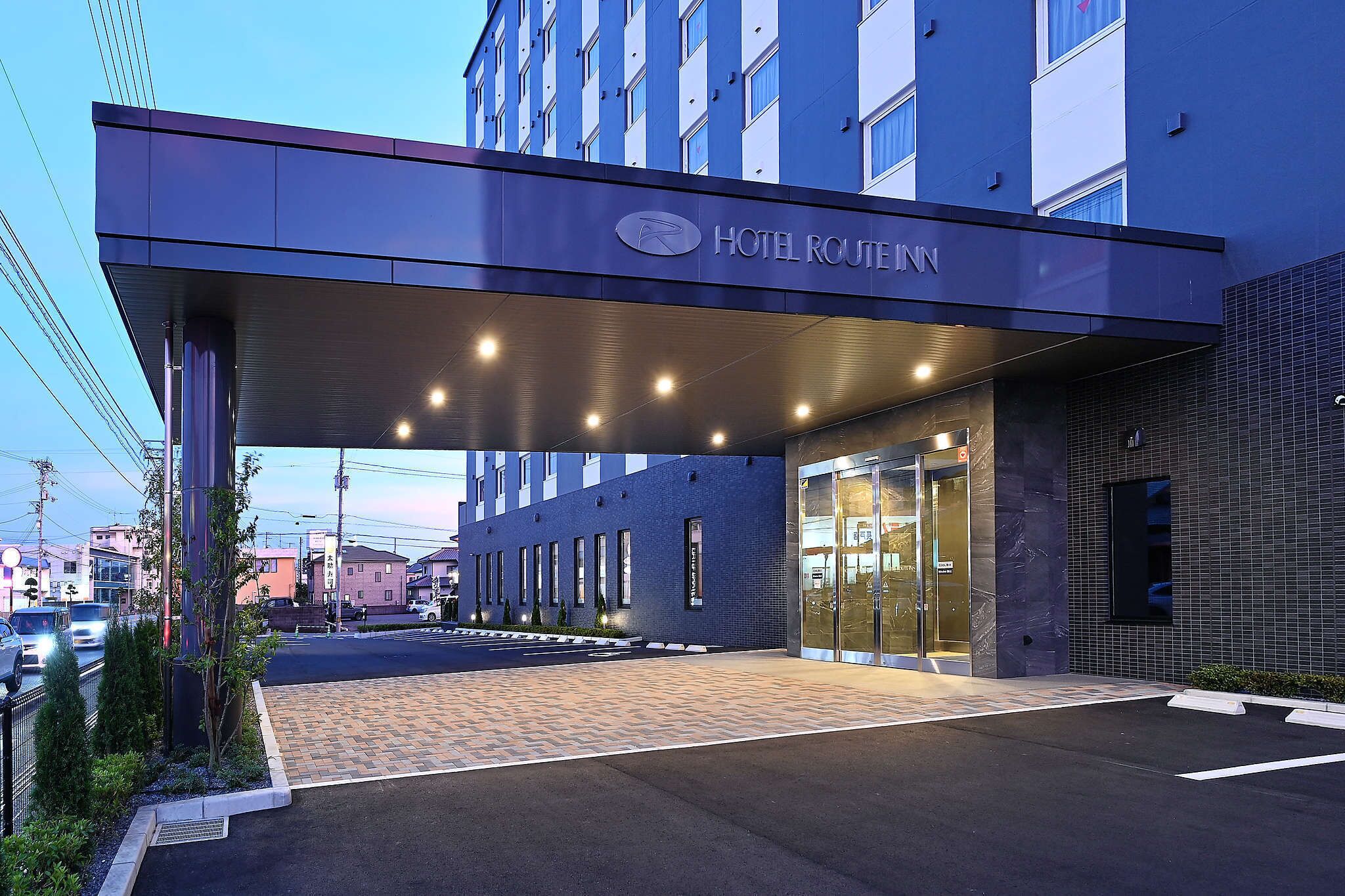 Entrada de hotel con un corredor cubierto, cielo despejado y zona de estacionamiento.