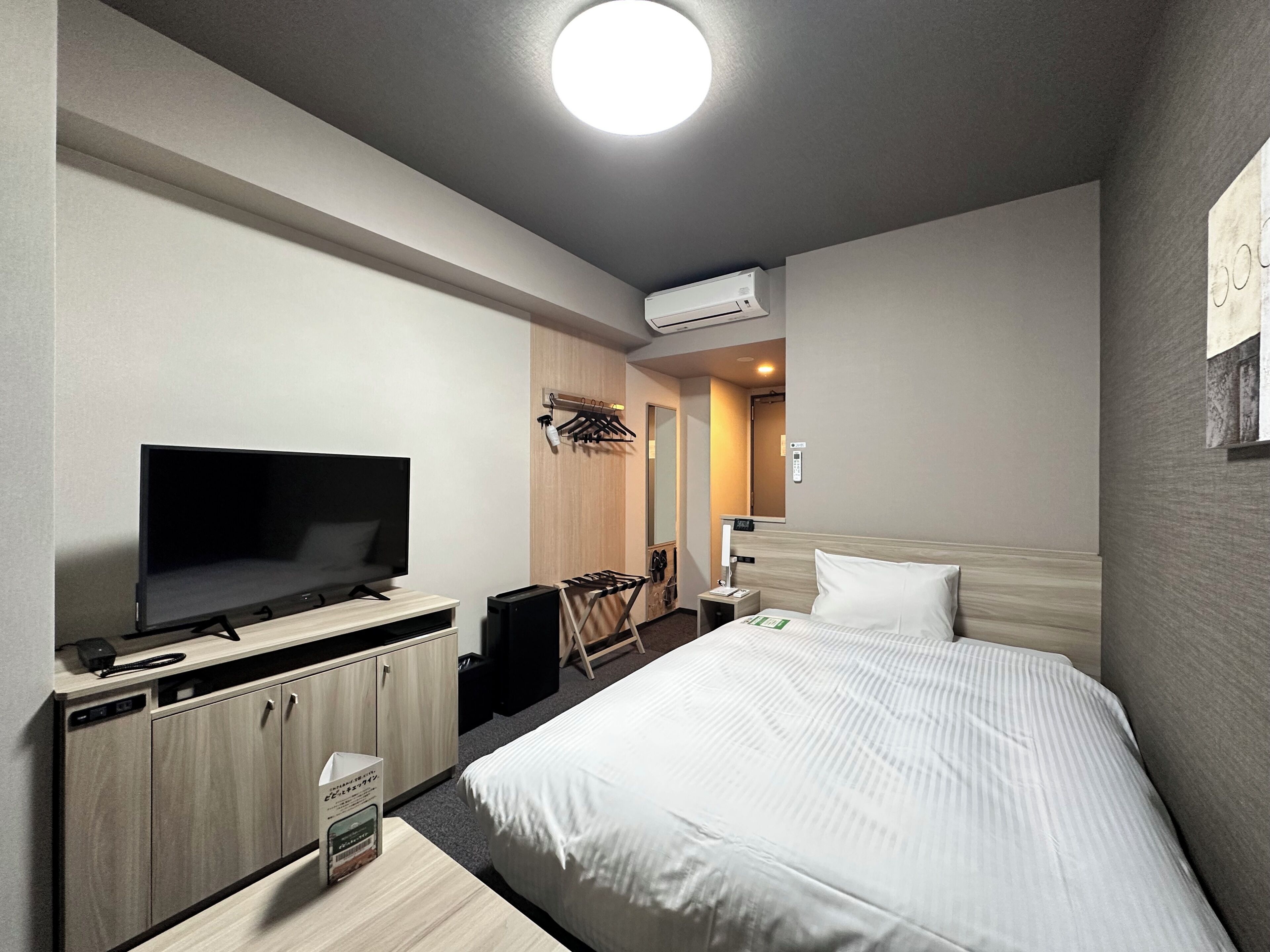 Habitación de hotel con cama, televisor, escritorio con computadora, armario y aire acondicionado.