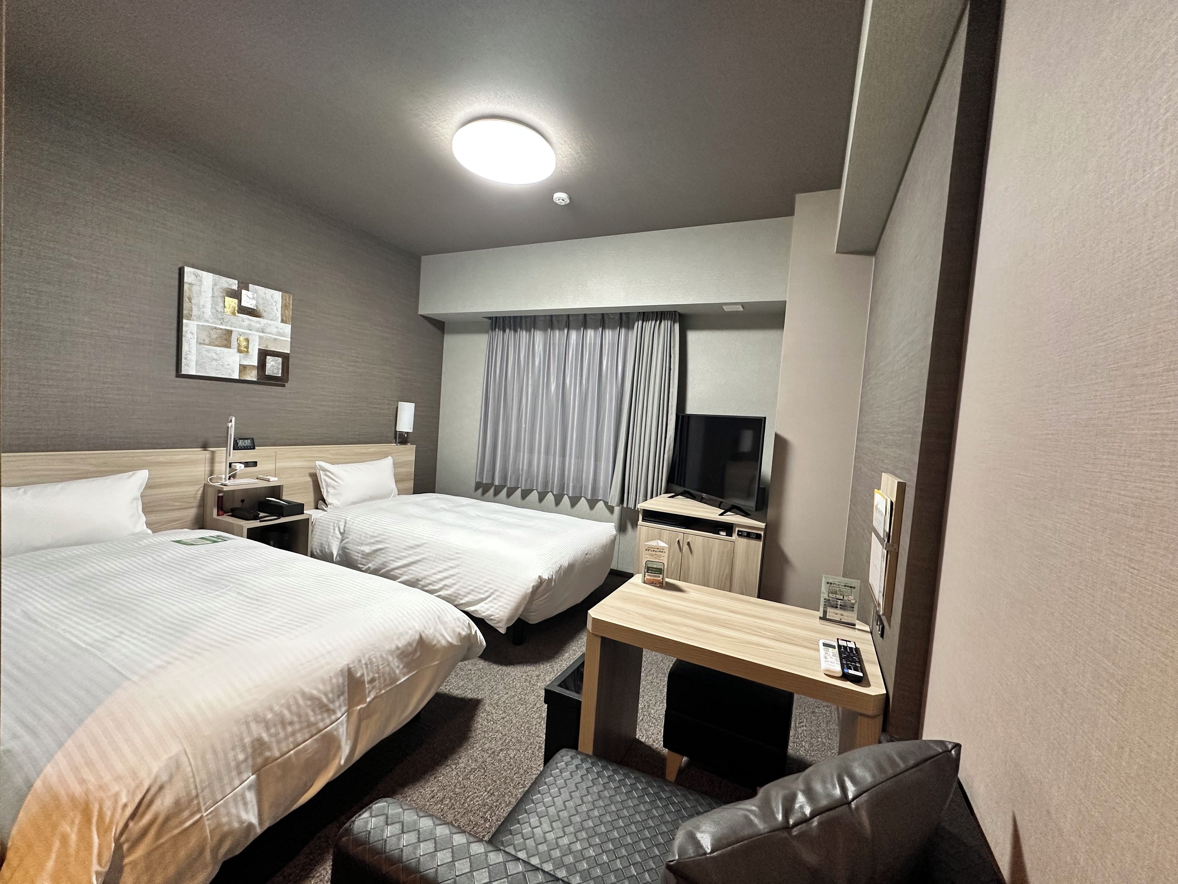 A hotel room with two beds, a desk, a television, and a small seating area.