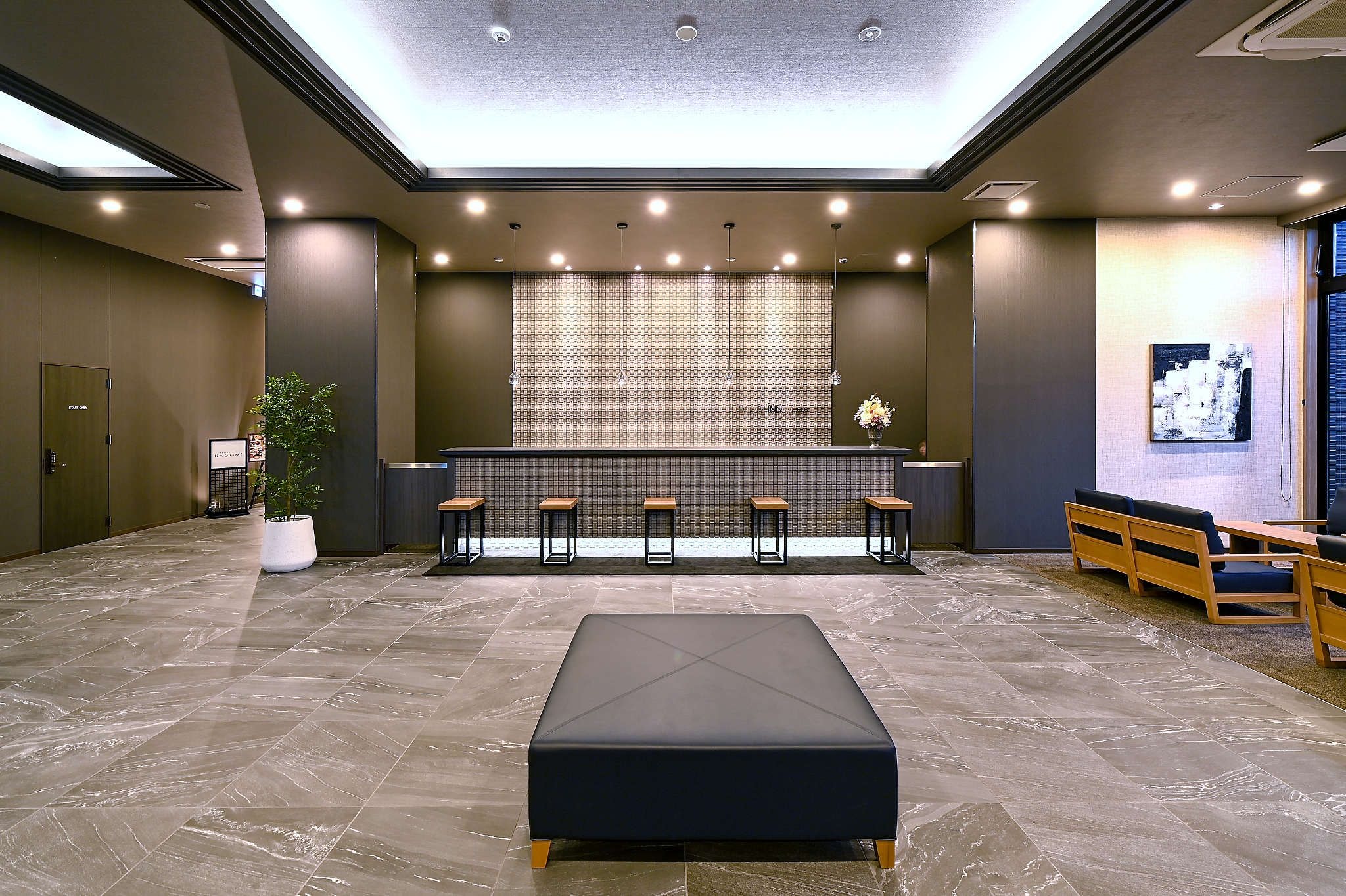 Eine moderne Lobby mit einer Rezeption, einer Sitzecke und einem großen schwarzen Pouf.