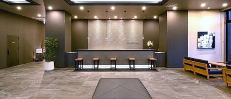 Um lobby moderno com balcão de recepção, área de estar e um grande banquinho preto.