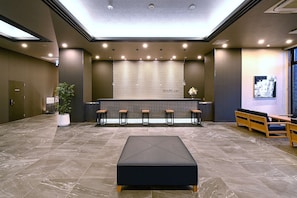 A modern lobby with a reception desk, seating area, and a large black ottoman.