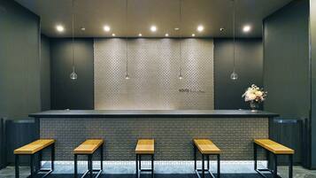 A bar area with a tiled backsplash, five wooden stools, hanging pendant lights, and a vase with flowers on the counter.