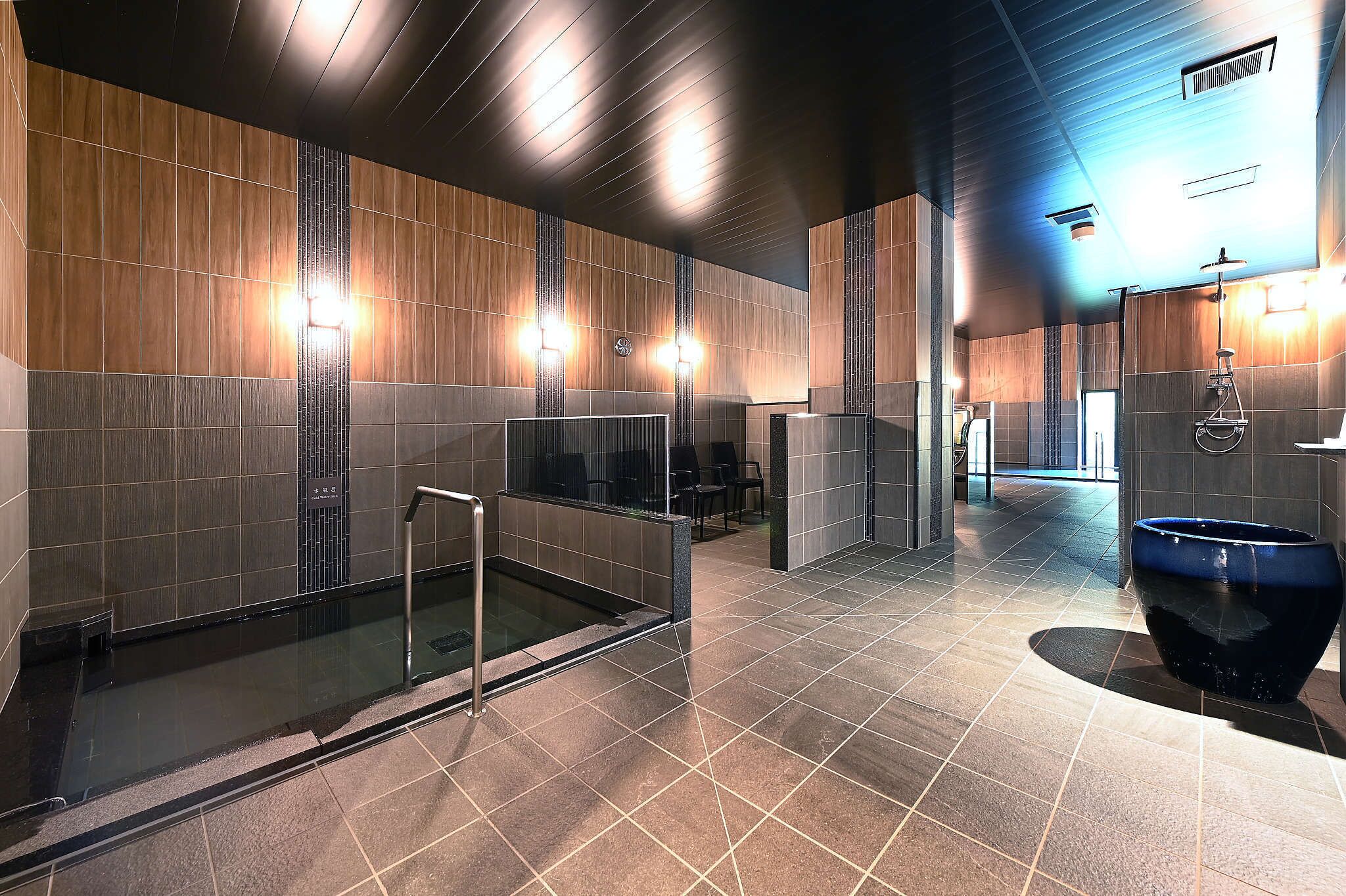 A modern bathroom with a glass-enclosed shower, a large blue basin, and a wall-mounted toilet.