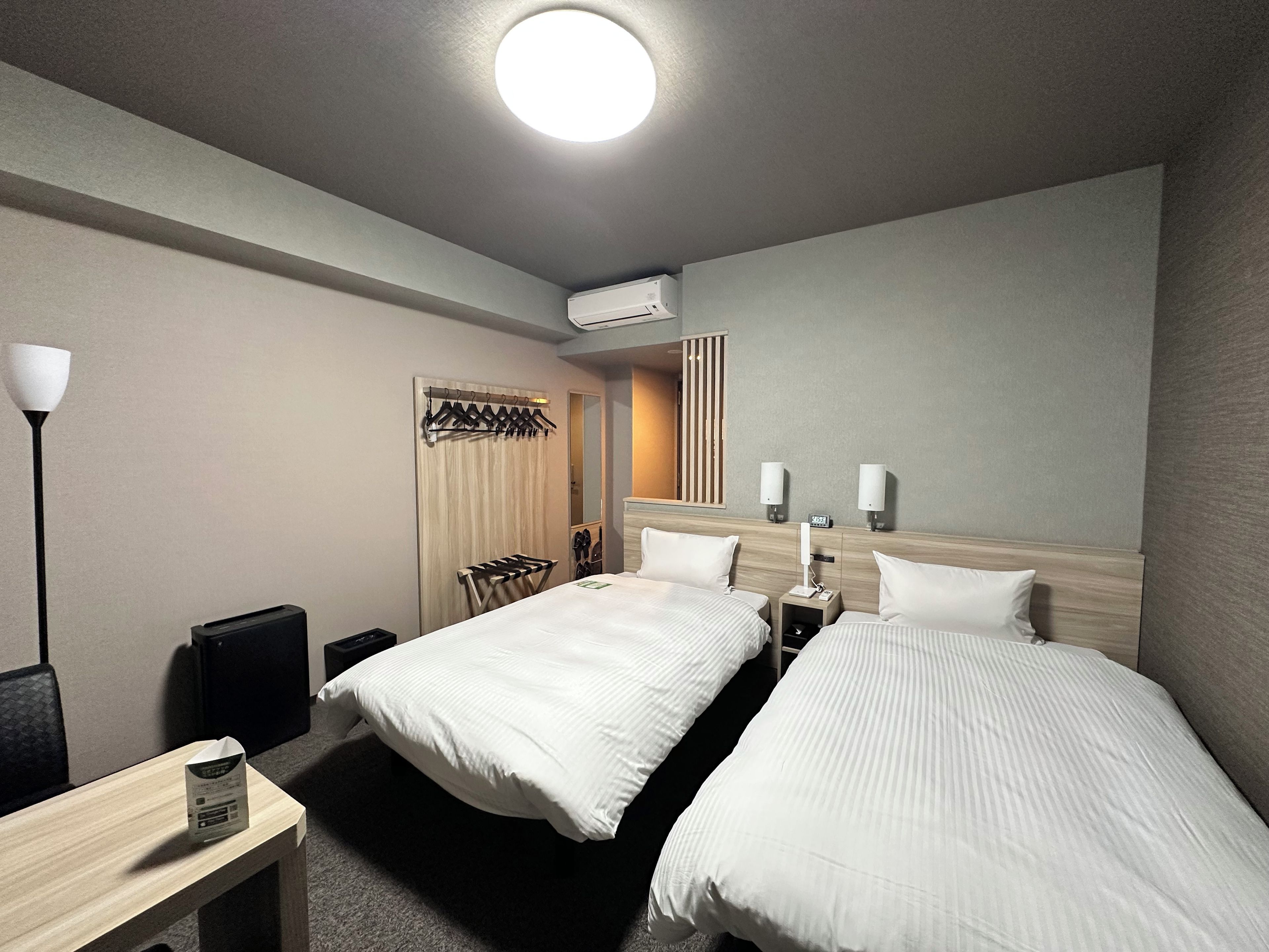 Habitación de hotel con dos camas, un escritorio con lámpara, armario y espejo.