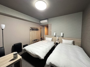 Habitación de hotel con dos camas, un escritorio con lámpara, armario y espejo.