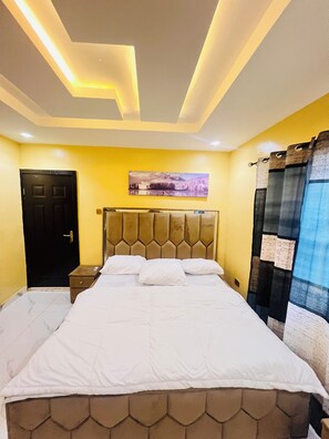 A hotel room with a bed, a headboard, a nightstand, a door, and a wall-mounted artwork.